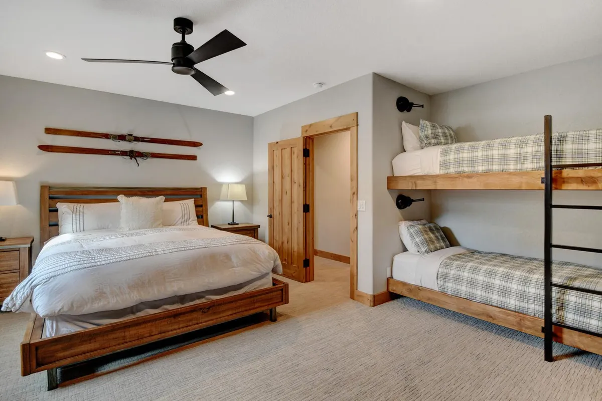A spacious interior bedroom featuring a king-size bed and a custom bunk bed, all framed by warm wooden decor and a ceiling fan. The room exudes a comfortable, family-friendly atmosphere, suitable for both parents and children. The cozy arrangements suggest the potential for both privacy and family bonding, with ample space and thoughtful details for restful nights and playful moments.