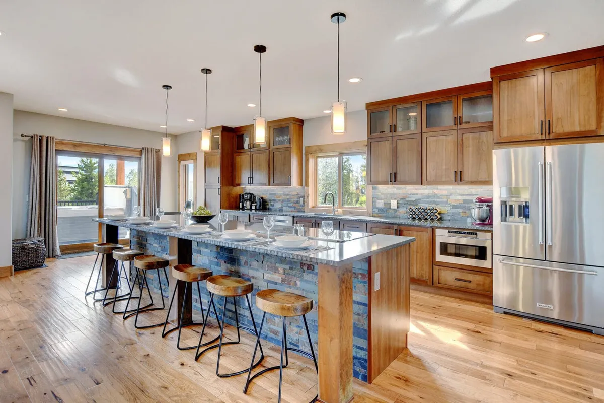 A spacious, welcoming kitchen with a large island featuring bar stools, sleek cabinetry, and wide windows. The view hints at both the kitchen's functionality for meal prep and its role as a social hub for casual dining and entertaining.