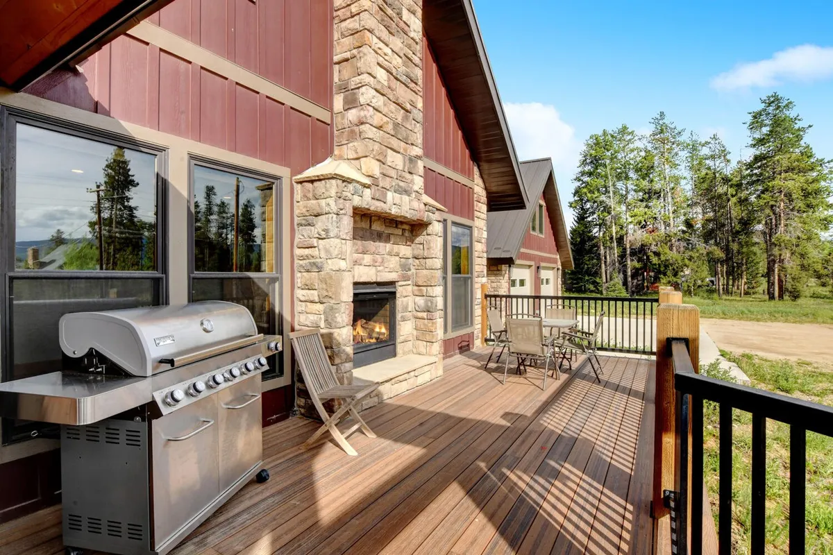 A welcoming deck setup with a professional gas grill, outdoor seating, and a double-sided fireplace. The deck is constructed of wood, complemented by cozy seating arrangements that encourage socializing, dining, and enjoying fireside warmth under the open sky.