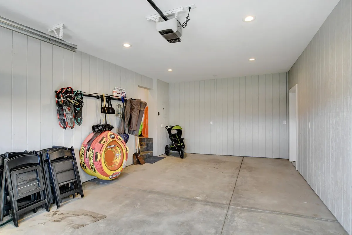 A practical yet inviting mudroom or storage area features hanging water sports equipment, colorful inflatable floaties, and a stroller, evoking preparation for warm-weather adventures and family excursions.