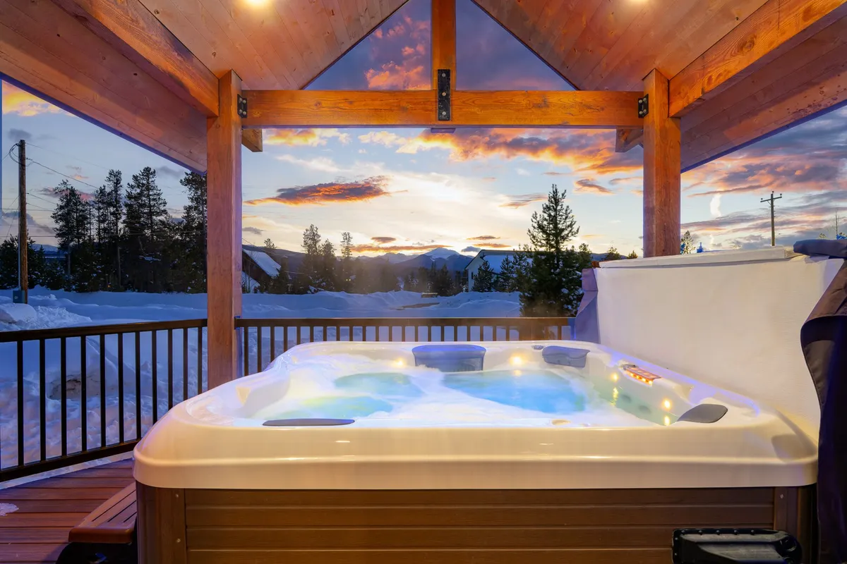 A serene outdoor scene featuring a private hot tub on a spacious deck overlooking sweeping mountain views as the sun sets. The bubbling water invites relaxation, while the surrounding natural beauty is visible in the background, blending the comforts of outdoor living with alpine scenery.