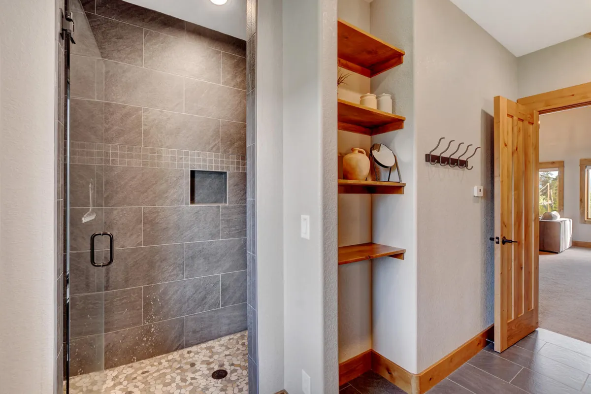A stylish bathroom with a glass shower enclosure, textured tiles, and wooden shelving, combining modern amenities with spa-like tranquility. The space is designed for relaxation and rejuvenation, echoing the feel of an upscale spa retreat.