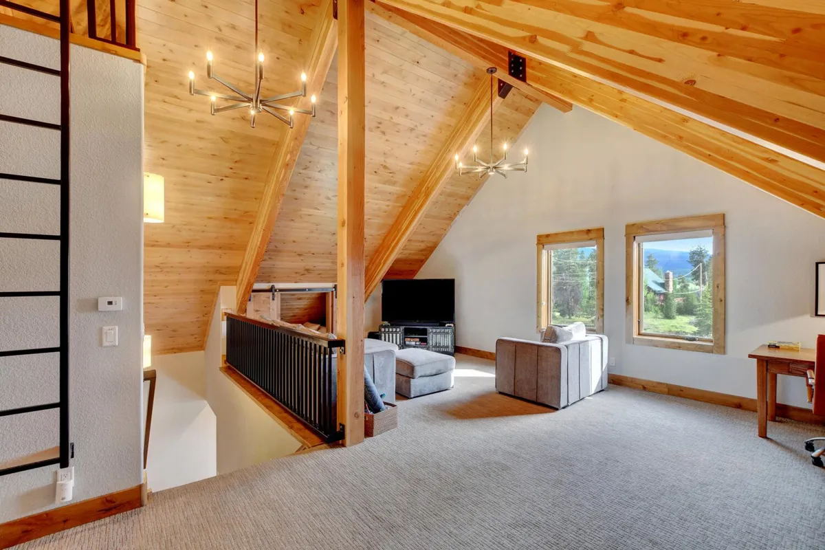 This image captures a welcoming living area with wooden beams, large windows revealing serene outdoor views, and a comfortable seating space. The room's warm lighting and cozy decor emphasize a retreat-like ambiance for unwinding and socializing.