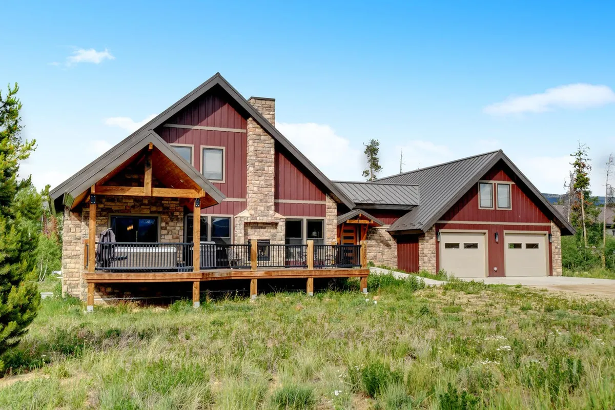 This exterior shot captures the home's inviting wooden deck, stone chimney, and vibrant red siding, set against a backdrop of natural surroundings. Large windows hint at the cozy interior, while the spacious porch suggests a perfect spot for relaxation or small gatherings.